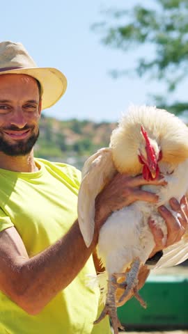 Smiling male farmer holding a white chicken in her farm