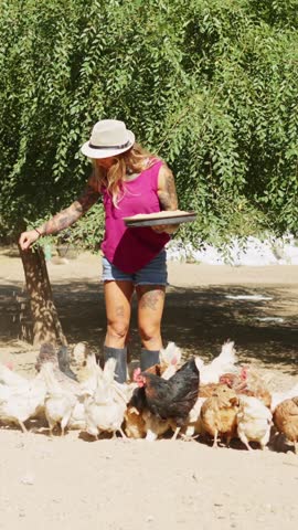 Tattooed female farmer feeding chickens and geese in a farm
