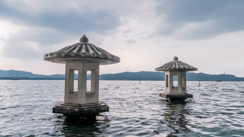 Traditional Chinese stone pavilions standing in West Lake waters with mountains in background, Hangzhou, China. Serene lakeside architecture perfect for travel content.