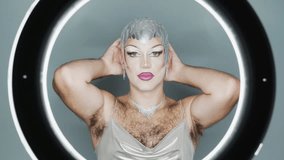 Confident latin drag queen with glamorous makeup and a silver futuristic outfit dancing and posing for the camera inside a circular light, showing a new concept of gender fluidity and expression - Powered by Shutterstock - Get 15% off with code: PIKWIZARD15