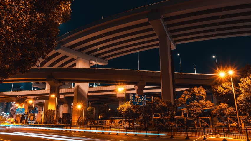 Time lapse night scene of Shanghai Nanpu Bridge with flying traffic light trails and illuminated urban infrastructure against dark sky