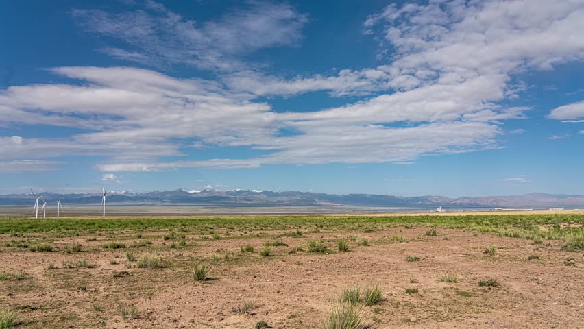 Time lapse footage of natural landforms in Qaidam Basin, Qinghai, China featuring vast desert terrain with wind turbines and dramatic cloudy sky over arid landscape.