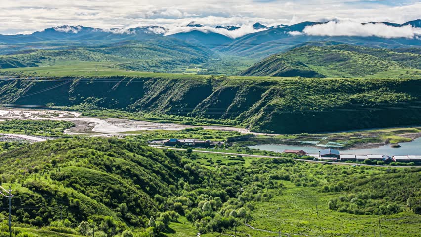 Time lapse video of dramatic mountain landscape with rolling green hills, rivers, and clouds in West Sichuan, China featuring scenic grassland terrain and valleys.