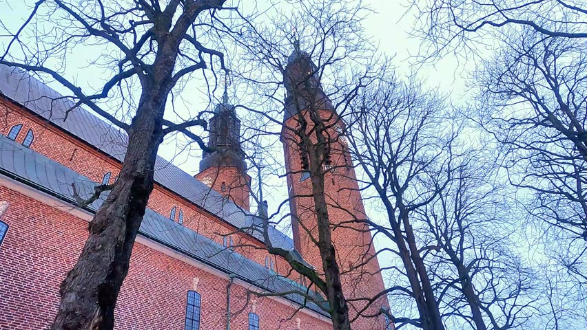 A look upward at the two towers of the famous church in Sodermalm, Stockholm. Hogalidskyrkan church is recognized by its two towers. Trees stand bare outside the huge building in the winter.