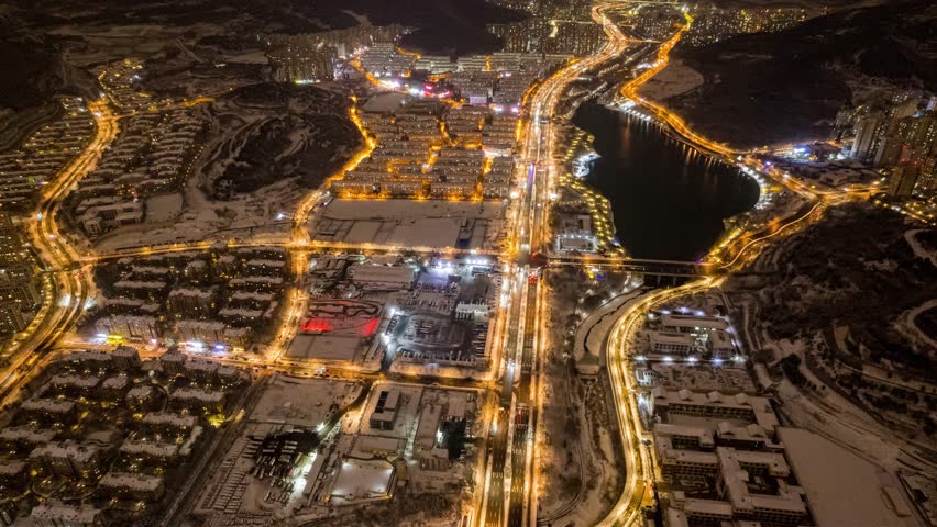 Aerial night view of Jinan city in Shandong province showing illuminated highways, traffic trails, and snow-covered urban landscape in winter time lapse style.