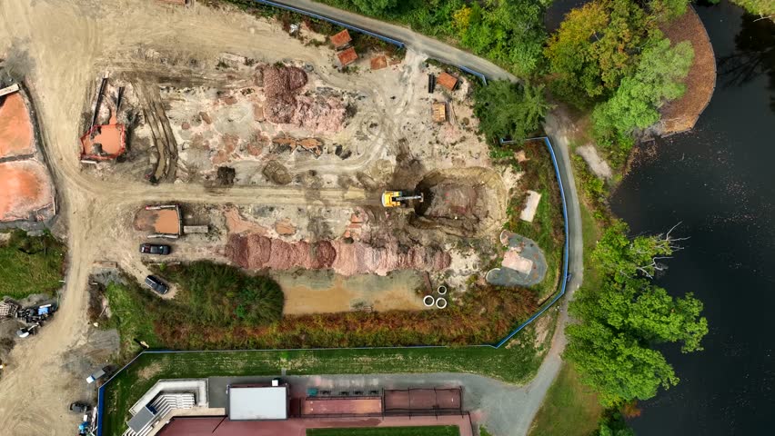 Aerial view of construction site near water with machinery and greenery