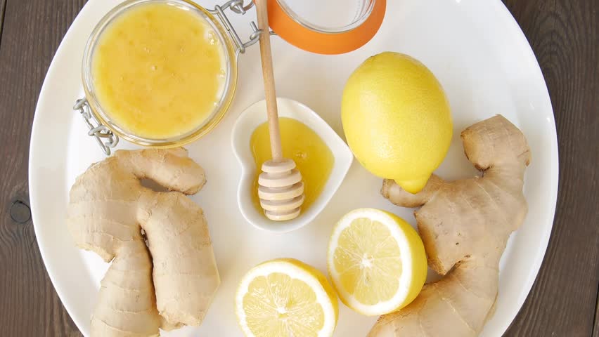 Natural remedy with fresh lemon, ginger and honey rotating on a plate.