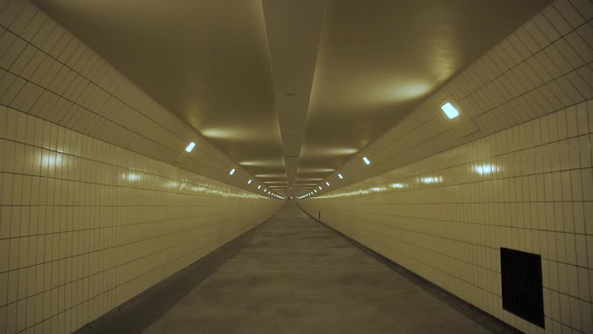 Dynamic push through view of long tiled pedestrian tunnel at train station in Amsterdam Netherlands showing symmetry perspective and soft yellow lighting creating cinematic urban atmosphere