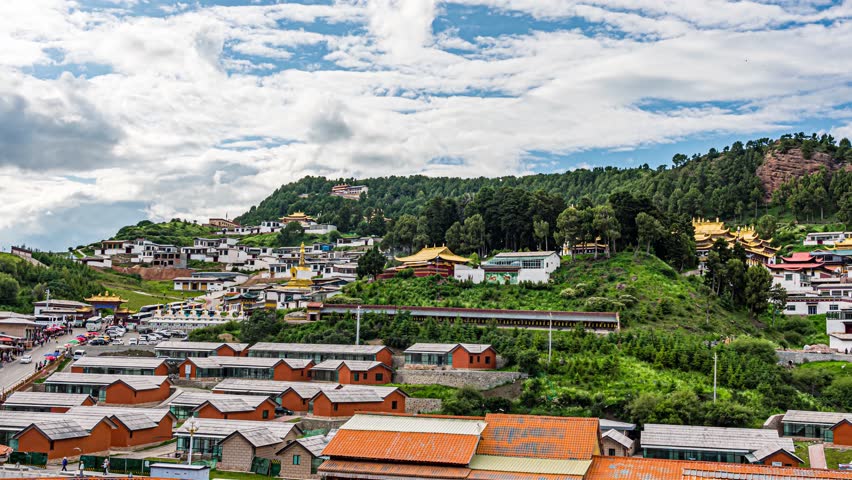 Aerial view of Ruoergai town nestled in green hills of Sichuan Province, China, showcasing traditional and modern architecture under dramatic cloudy sky.
