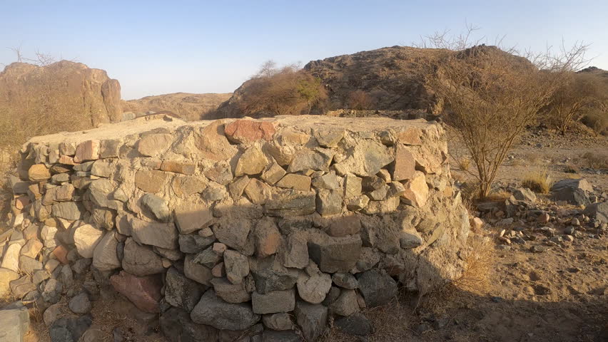 Close-up, atmospheric shot of a circular dry-stone well structure in rocky desert hills with distant mountains under a bright sky — ideal stock B-roll for landmarks, travel, archaeology projects.