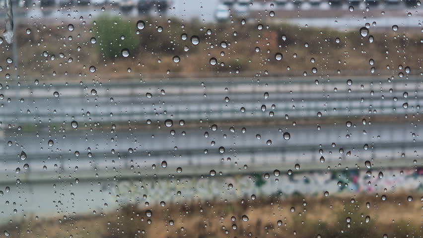 Moody view through a rain-covered window overlooking a road with passing cars in rainy day