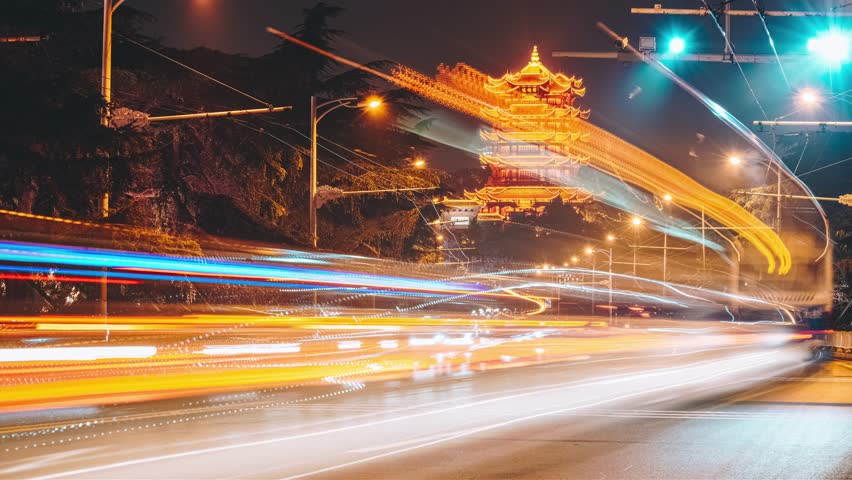 Time lapse night scene of Yellow Crane Tower in Wuhan with colorful light trails from traffic creating dynamic streaks across the historic Chinese landmark.