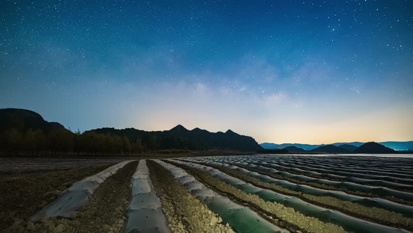 Stunning Milky Way galaxy stretching across starry night sky over Haifeng wetland agricultural fields in Yunnan, China with mountain silhouettes at dawn