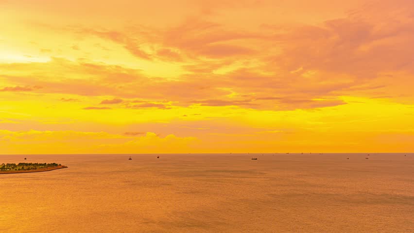 Stunning golden sunset over calm ocean waters with dramatic orange and yellow sky clouds reflecting on the sea surface during dusk time