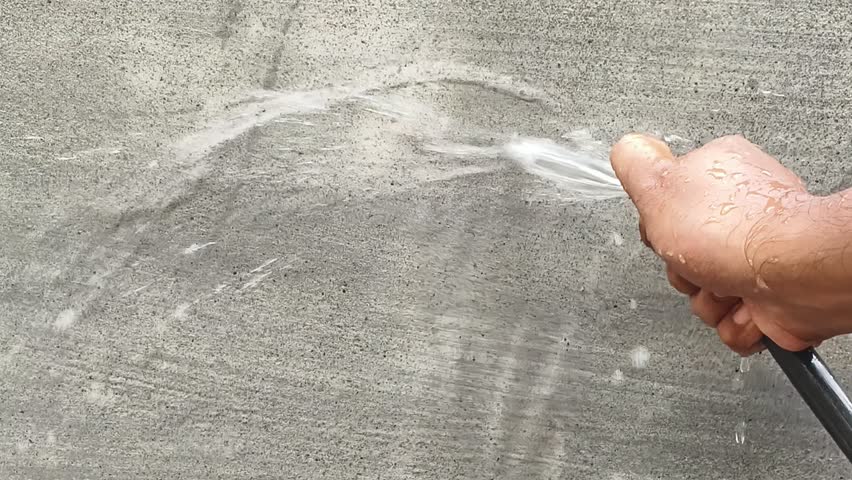 Closeup of Indian person hand with garden hose pouring water to wet new building cement wall surface after initial construction for preventing cracks, adding strength and stop curing.