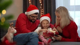 Father mother and little child in red santa hats open gift box with magic light next to christmas tree at home. Happy family celebrate Christmas New Year - Powered by Shutterstock - Get 15% off with code: PIKWIZARD15