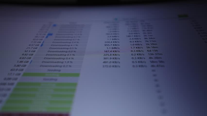 Shooting from below of computer screen showing p2p client interface with close-up of multiple files downloading and uploading, real-time transfer speeds, progress bars, status indicators, slow motion