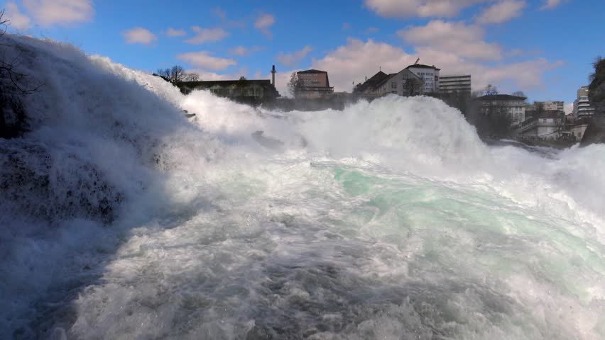Water falls and drops scatter in different directions on Rhine Falls against old town in Switzerland