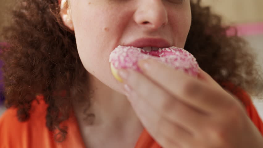 Young woman biting donut, enjoying sweet dessert, unhealthy eating habits