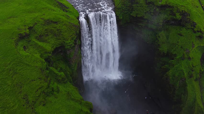 Skogafoss waterfall flowing through green cliffs in Iceland.  4k aerial slow motion view of epic waterfall, Skogafoss waterfall - one of the most popular waterfalls in Iceland.