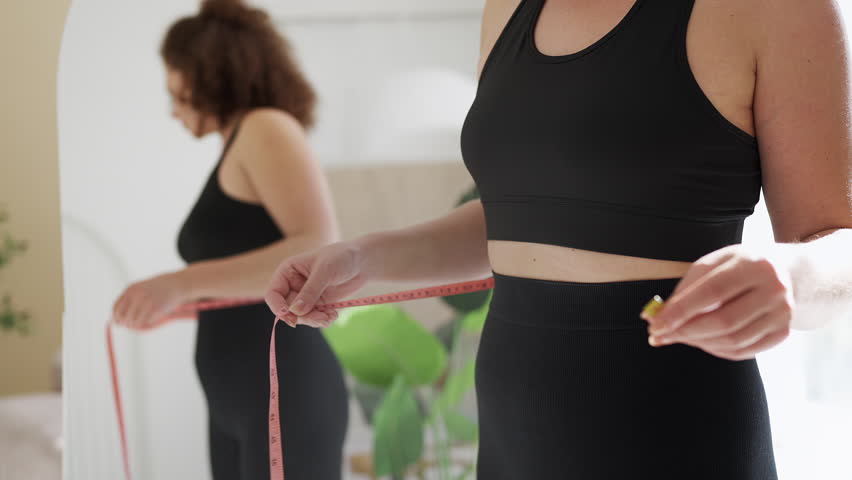 Young woman measuring waist with tape, unhappy with her body looks, diet stress