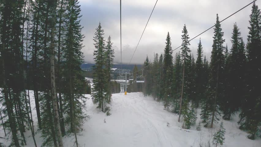 Aerial view of a scenic ski trail winding through a snowy mountain landscape in Banff National Park, Canada. The winter scene captures crisp white slopes surrounded by dense pine forest in cloudy day	