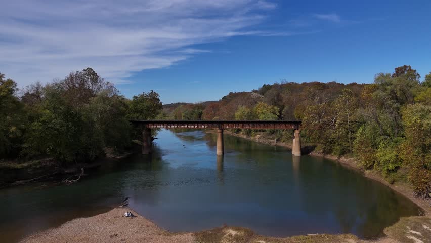 Aerial view of the Rail Bridge over the clear Meramec River, with trees lining the riverbanks under a bright blue sky, Ballwin, Missouri, United States.