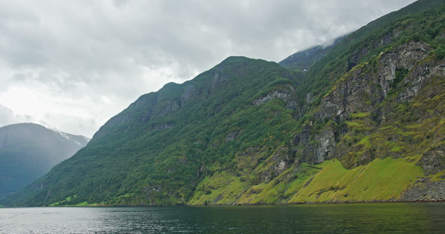 Norway fjord mountains with lush green cliffs along calm water near Naeroyfjord and Aurlandsfjord, wide scenic landscape under an overcast sky