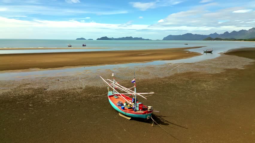 Aerial view of a colorful fishing boat stranded on a vast expanse of muddy beach with the ocean in the background, Sam Roi Yot, Prachuap Khiri Khan, Thailand.