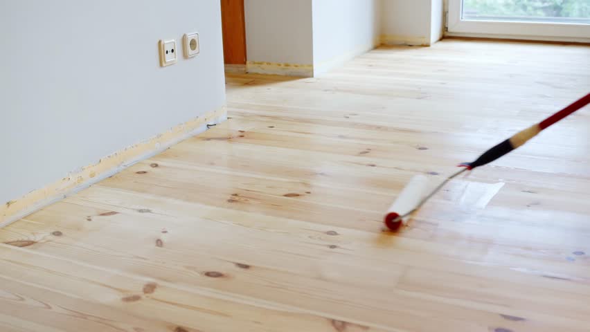 A professional applying transparent protective coating on freshly installed hardwood flooring using a roller tool in an indoor residential renovation project showcasing DIY home improvement techniques