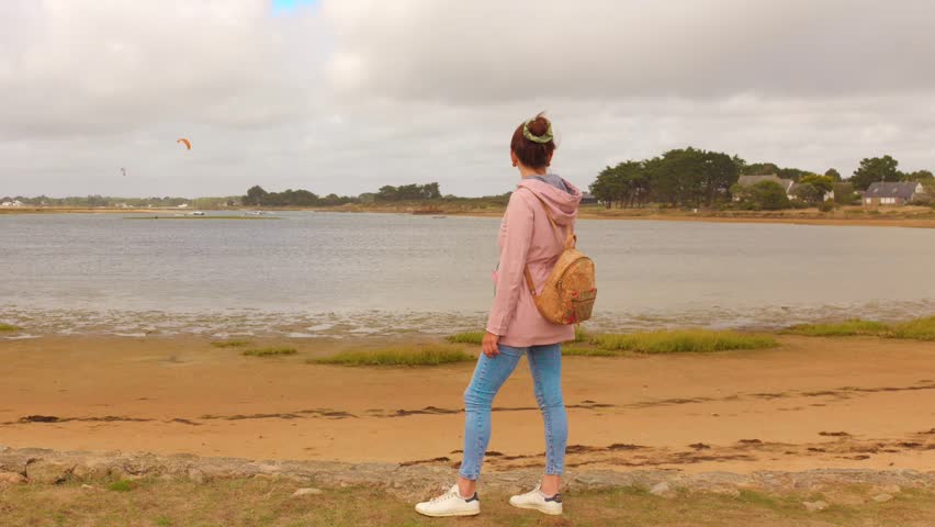 Woman by beach in Brittany, France with kite surfers in background