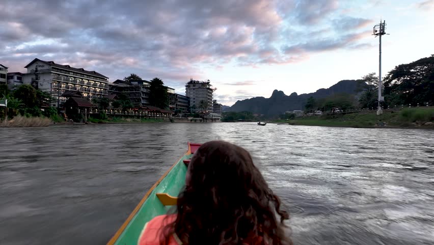 A passenger in a long-tail boat glides along Nam Song River toward scenic karst mountains at sunset.