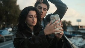 Couple poses for a selfie with a smartphone near a harbor at sunset, capturing a relaxed and joyful moment together. - Powered by Shutterstock - Get 15% off with code: PIKWIZARD15