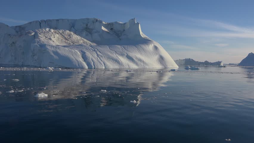Icebergs drift serenely in clear blue Arctic waters. The sun shines brightly, reflecting off the ice. A beautiful scene of nature's wonders in the Arctic landscape.