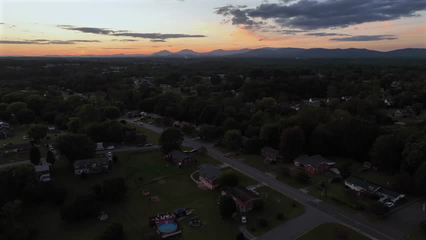 Aerial wide shot of dusk scene in american suburb neighborhood after sunset time. Mountain range in distance. Driving car one straight street.