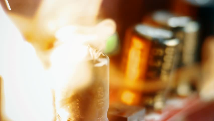A burst capacitor in flames on a motherboard, extreme close-up. Catastrophic electronic failure due to overheating or high voltage. Danger of short circuit and technical malfunction.