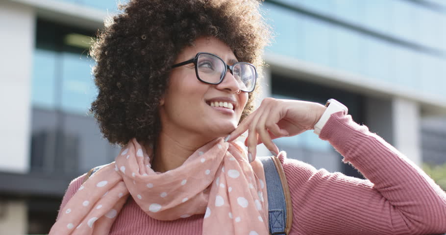 African American woman in plaza, breeze lifting scarf while adjusting eyeglasses, savoring air. Urban, modern, fashion, casual, confidence, outdoors, lifestyle