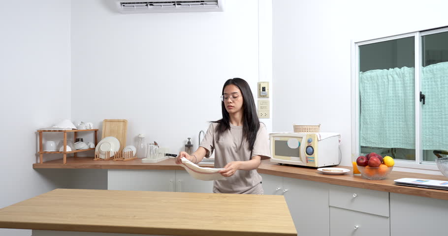 asian young woman cleaning kitchen counter with cloth during quiet weekend morning at home showing simple domestic lifestyle and responsibility in modern space with independence and care
