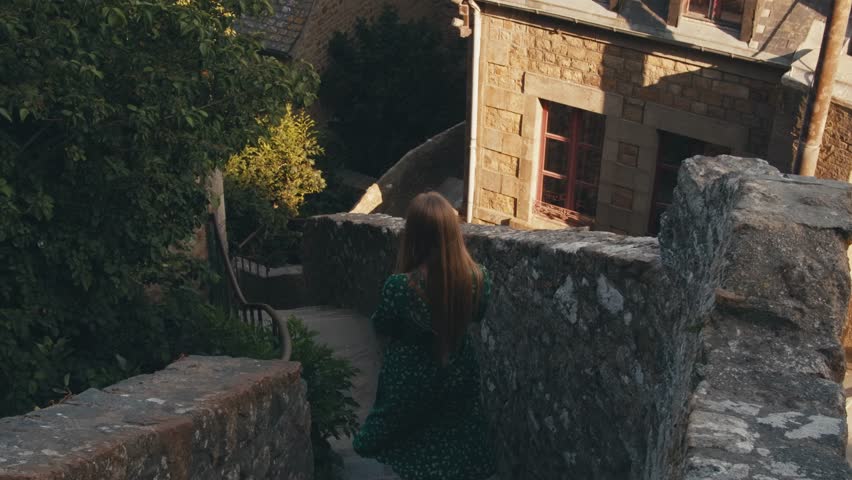 happy young woman tourist traveler in hat walking through streets steps of saint michel castle. Abbey Mont Saint-Michel Normandy France. view from inside fortress city. ancient architecture walls
