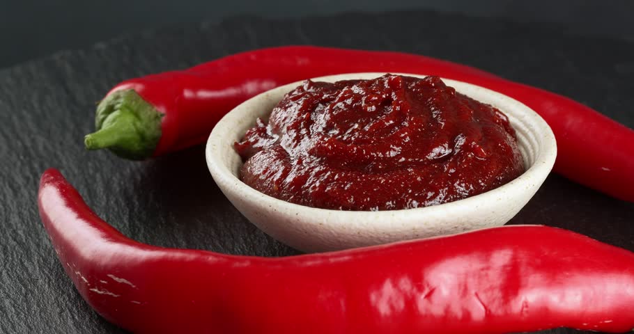 Bowl with spicy gochujang paste and fresh chili peppers. Close-up footage on a rotating table