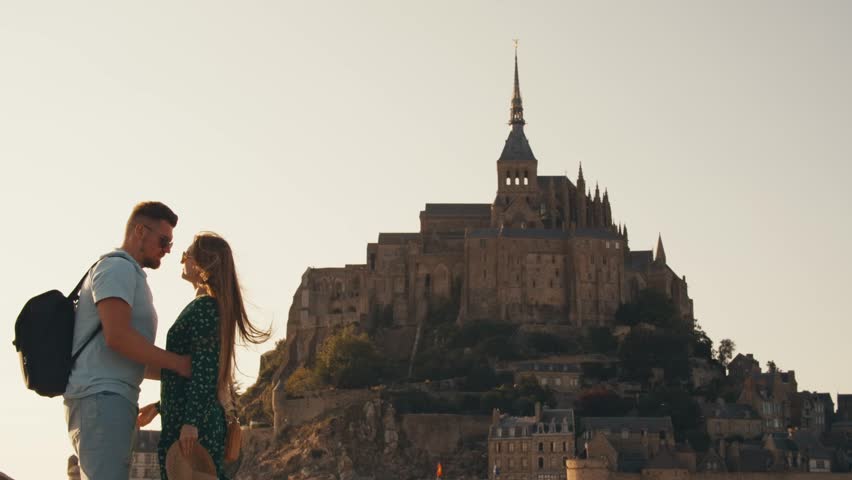 happy couple tourist traveler at background saint michel castle, hair blowing in wind. Abbey Mont Saint-Michel Normandy France. view from outside fortress city. man and woman hugging and kissing