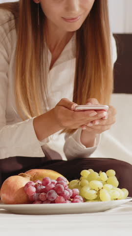A young woman with long hair smiles while looking at her phone. She is wearing a white shirt.