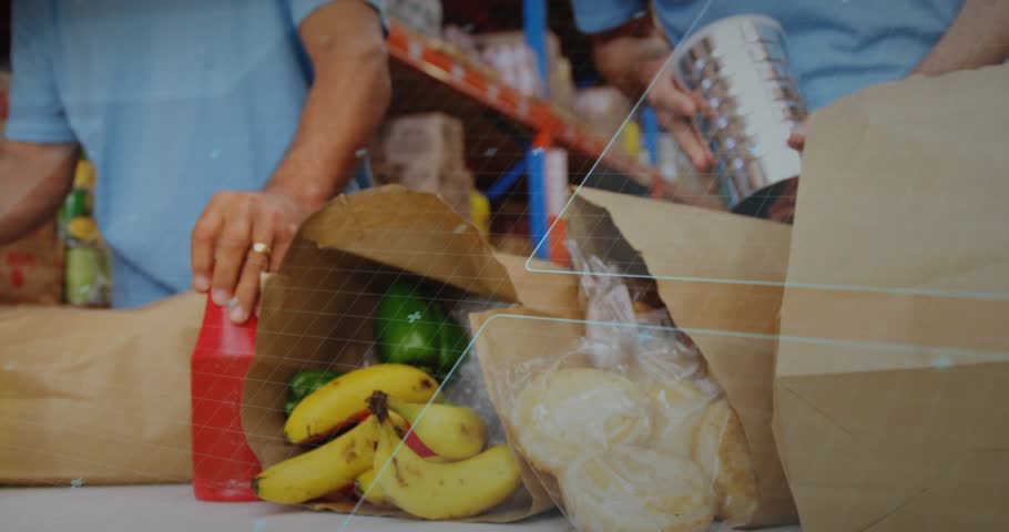 Hands arranging groceries initiating pullback, two volunteers packing while HUD aiding food packing. Warehouse, distribution, workers, collaboration, teamwork, organization, pallets
