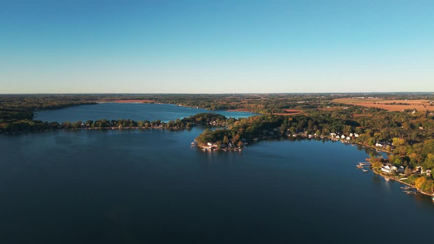 Drone aerial of freshwater bodies of water at Twin Lakes, Wisconsin summer vacation landscape during sunny  and warm early morning day above blue fresh water, homes, boat docks, and forest tree woods