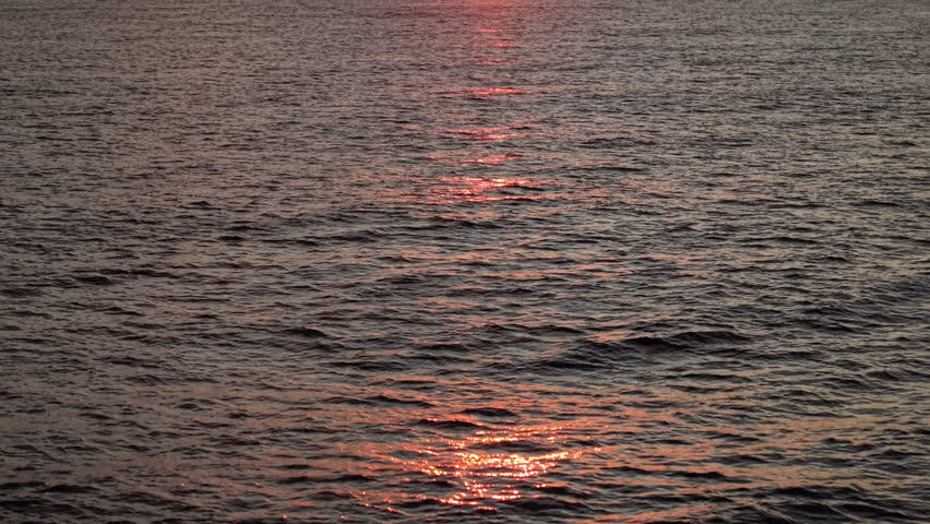 Drone flying low over the sea during sunrise, capturing gentle waves with glowing reflections before rising to reveal the colorful sky and the rising sun. High quality 4k footage