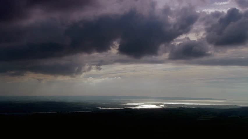 Dramatic clouds over a distant landscape with sunlight reflecting on the water