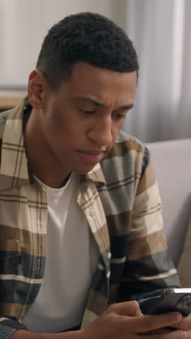 Upset sad frustrated African American man guy negative mood problem with mobile phone at home male confused disappointed thinking receive bank reject bad news finish stop using smartphone indoors