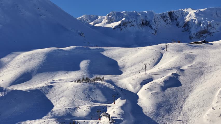 Aerial footage of snowy mountain slopes with tracks from skiers and snowboarders, along with active chairlifts in a bright winter landscape.