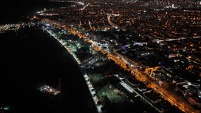 Aerial drone view over a coastal city at night, shimmering streets and skyscrapers meeting the dark ocean with a lit waterfront boardwalk and traffic lined coastal highway - Powered by Shutterstock - Get 15% off with code: PIKWIZARD15