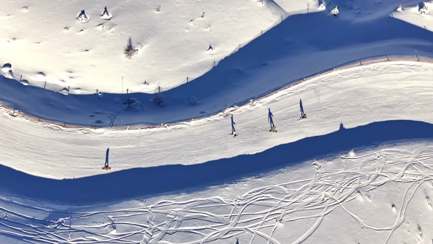 Aerial footage of skiers and snowboarders gliding down a snowy mountain slope, showcasing smooth winter sports action on a wide, sunlit piste.